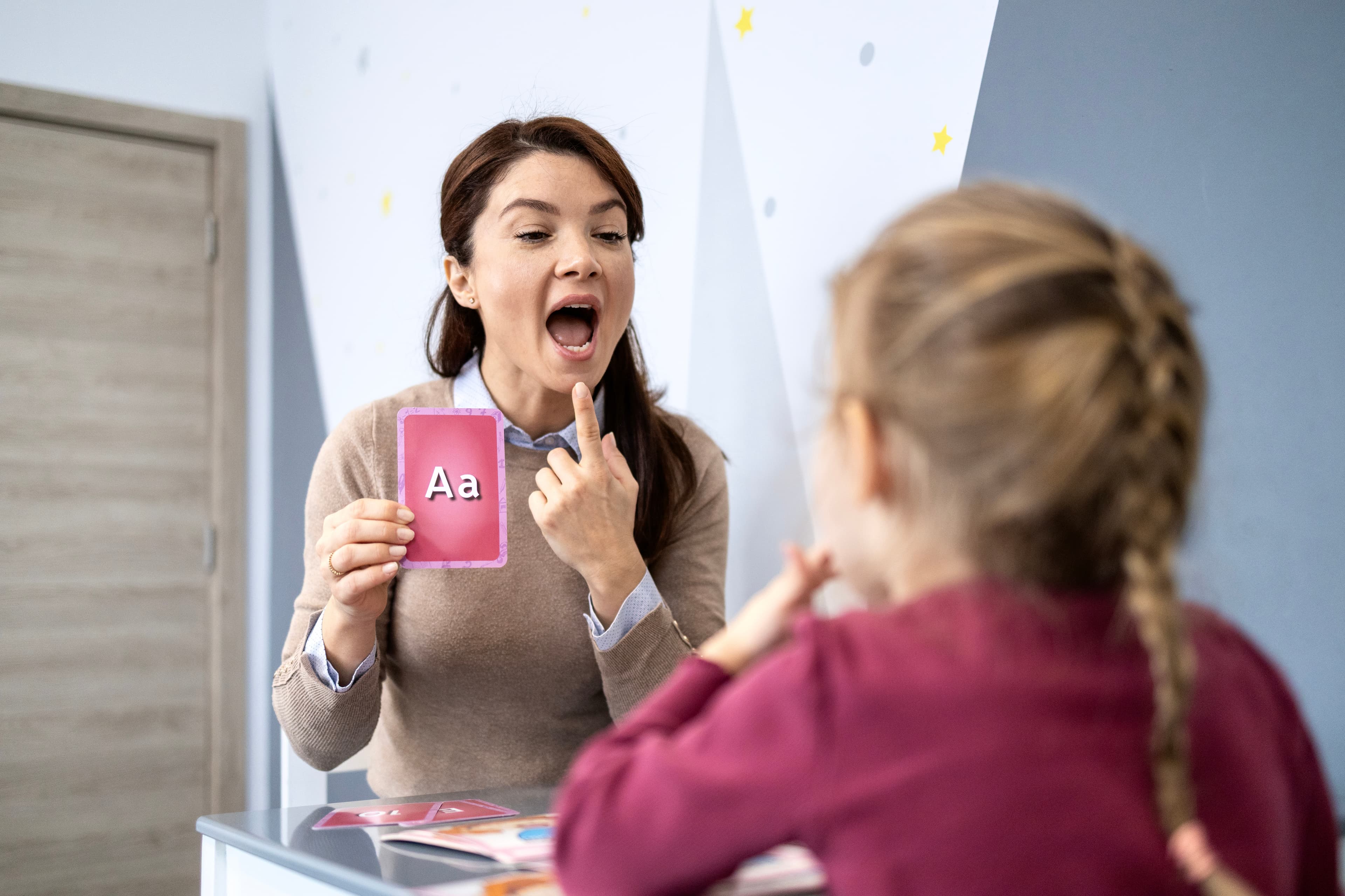 A speech therapist holding up an "Aa" flashcard while working with a child