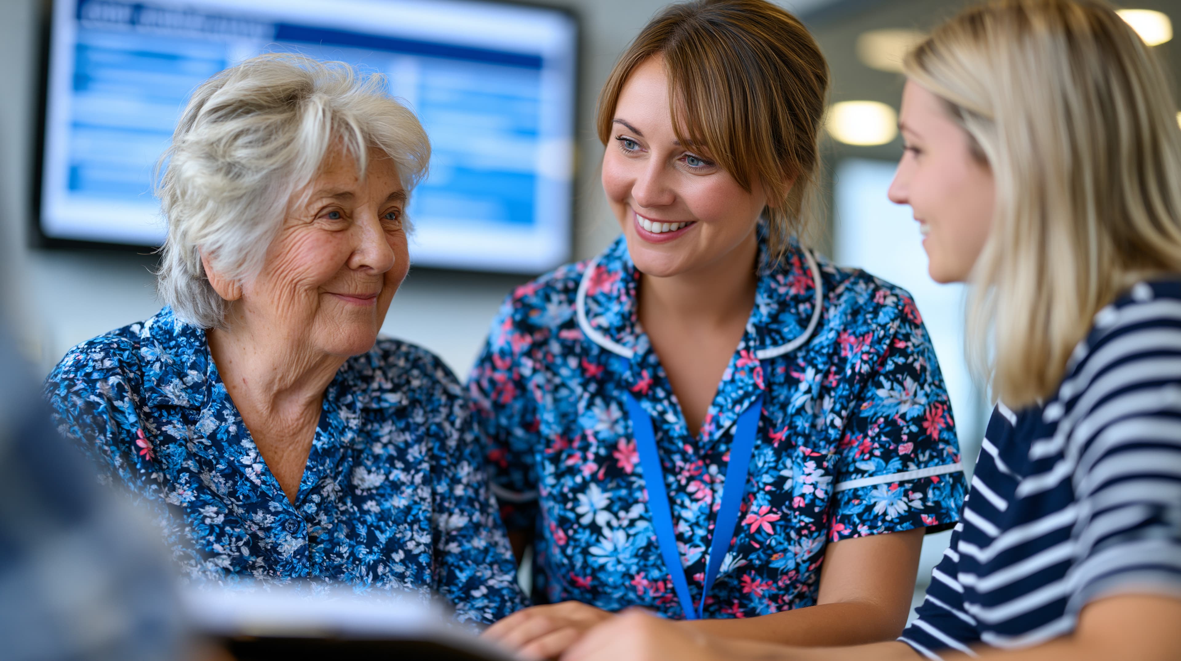 An older woman, a nurse, and a younger woman gathered together around a screen at a table